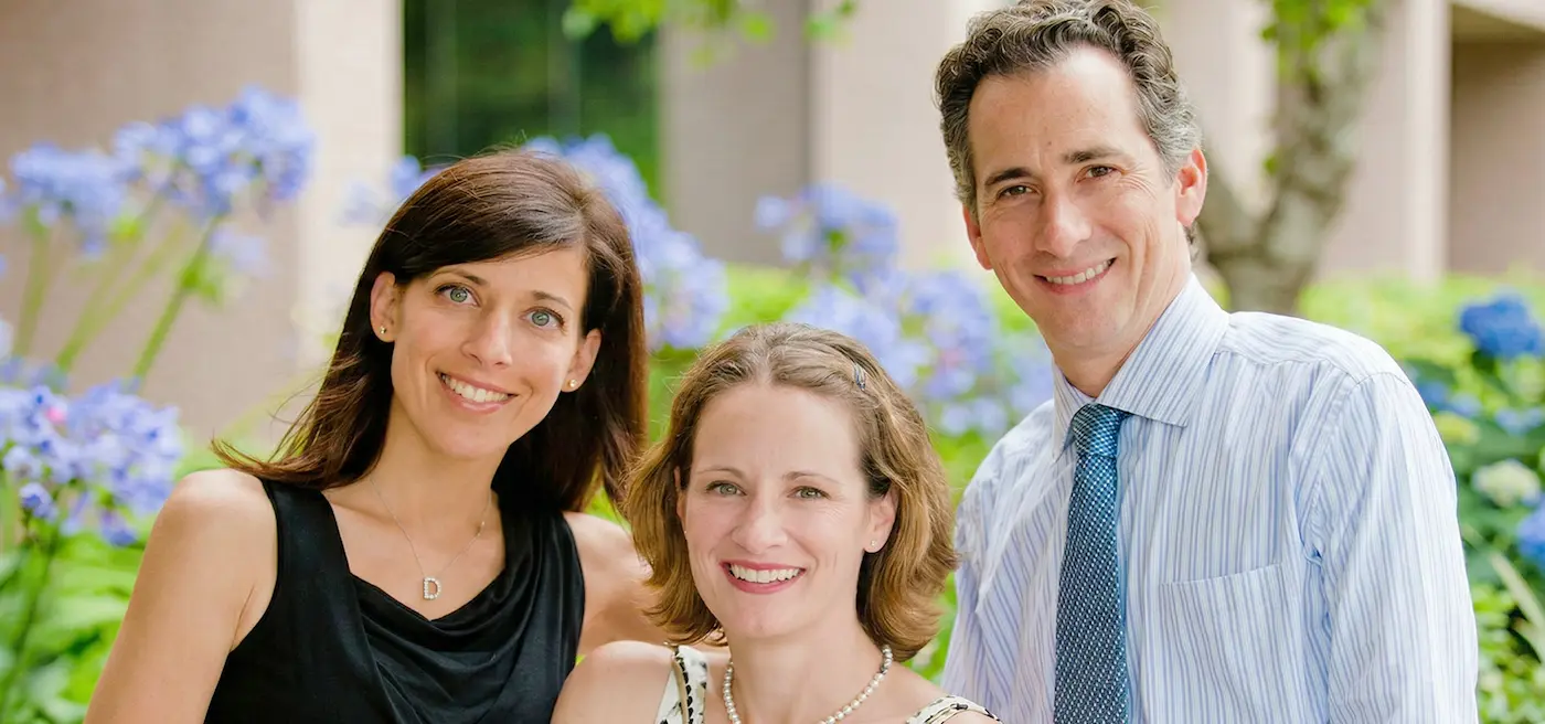 3 people standing together in front of flowers smiling